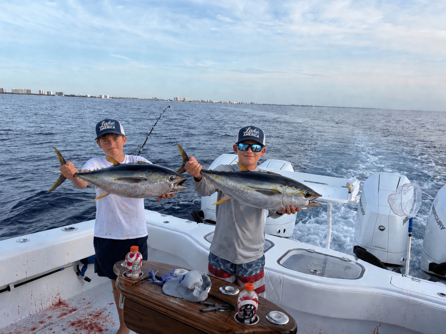 Two young anglers wearing Lake America hats while holding tuna on a fishing boat